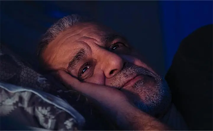 middle aged man laying awake in bed in a dark room